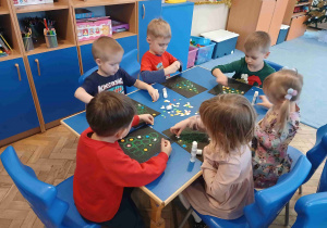 Dzieci wykonują prace plastyczną przy stolikach.