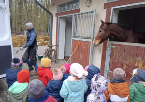 Dzieci obserwują jak kowal przygotowuje podkowę dla konia.