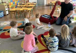 Dzieci siedzą na dywanie i biorą udział w zajęciach muzycznych.