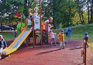 Dzieci bawią się na sprzętach w ogrodzie przedszkolnym.