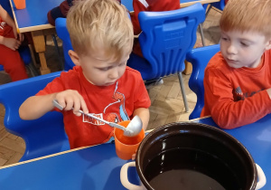 Chłopiec wlewa napój do kubka za pomocą chochli.