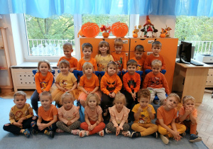 Grupa Motylków pozuje do zdjęcia w pomarańczowych strojach.