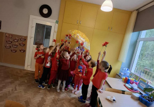 Dzieci prezentują wykonane przez siebie czerwone kwiaty.