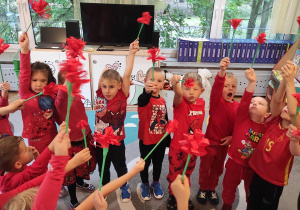 Dzieci podnoszą do góry czerwone kwiaty.