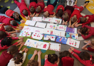 Dzieci prezentują wykonane przez siebie rysunki, leżąc w kole.