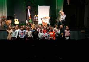 Żabki pozują na tle wielkiej sceny teatru i aktorów.