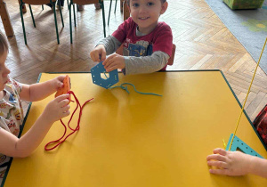 Dzieci przewlekają różne figury za pomocą sznureczków.