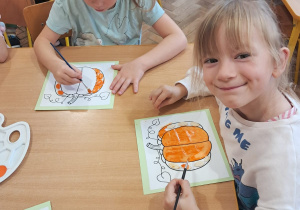 Dziewczynki malują farbami kontury dyni.