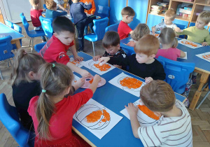 Dzieci wyklejają kontur dyni bibułą.